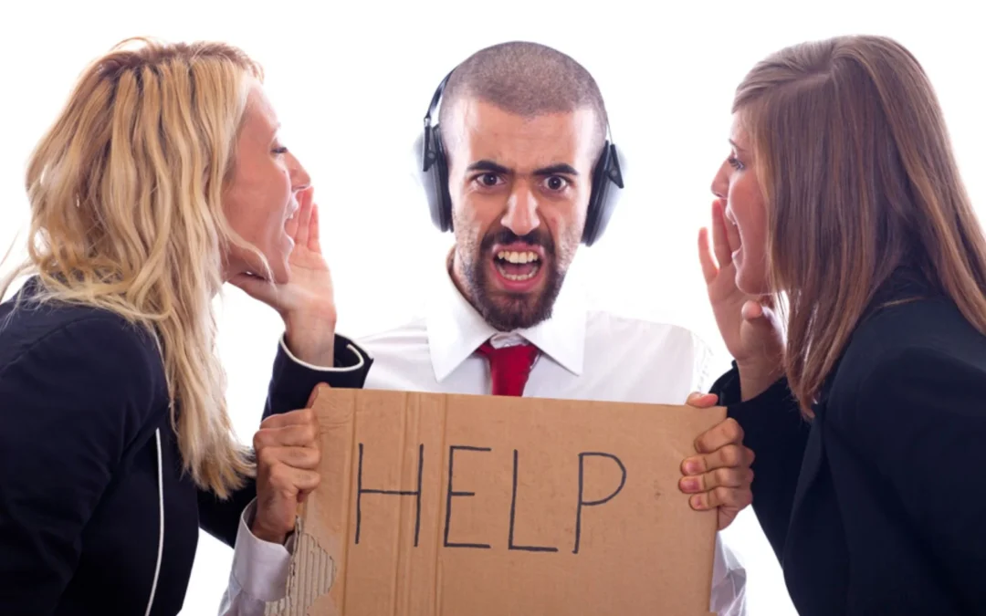 person wearing headphones and holding up sign saying 'help' while two colleagues yell