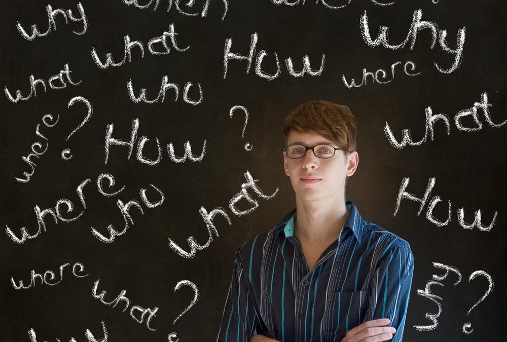 person standing in front of a blackboard with 'who, what, when, where, how' written all over it