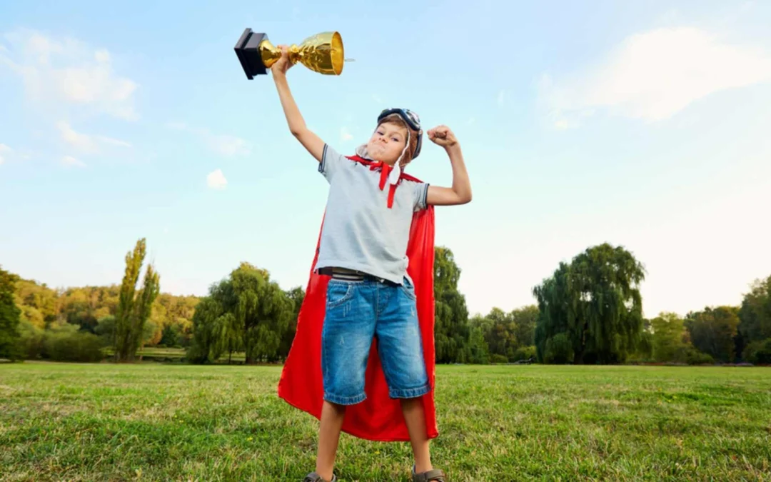 Kid wearing a cape holding a giant trophy