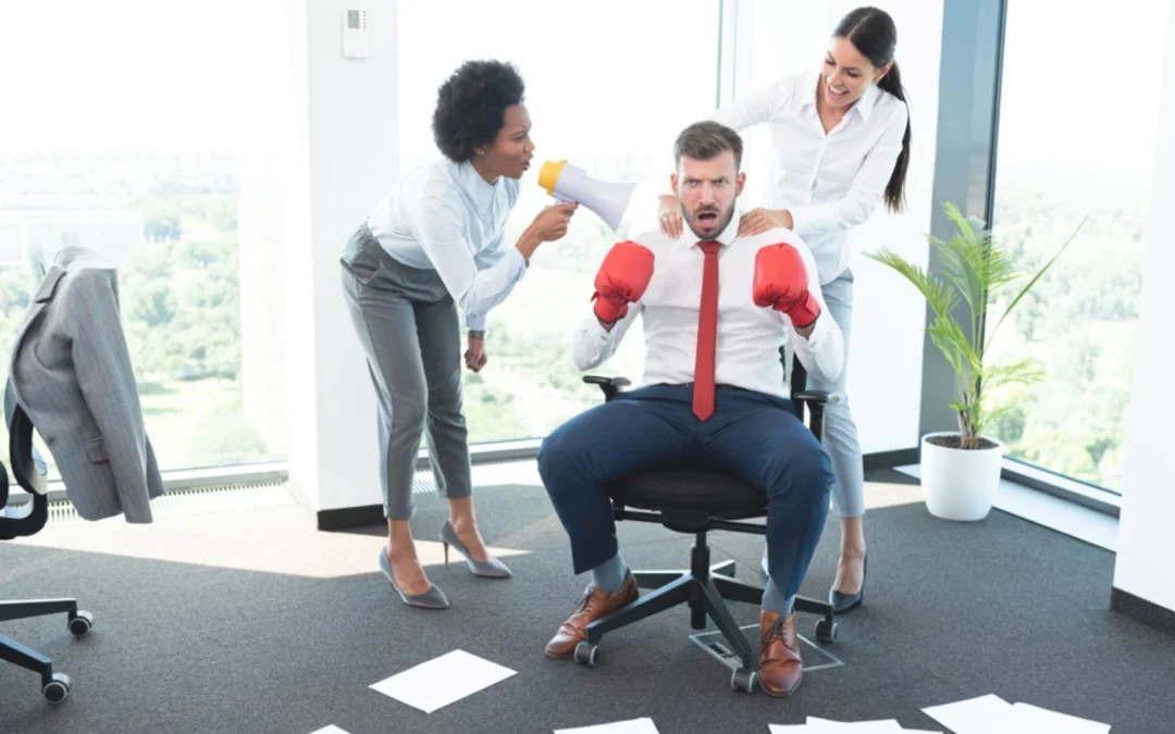 Business man wearing boxing gloves while female colleagues encourage him to fight