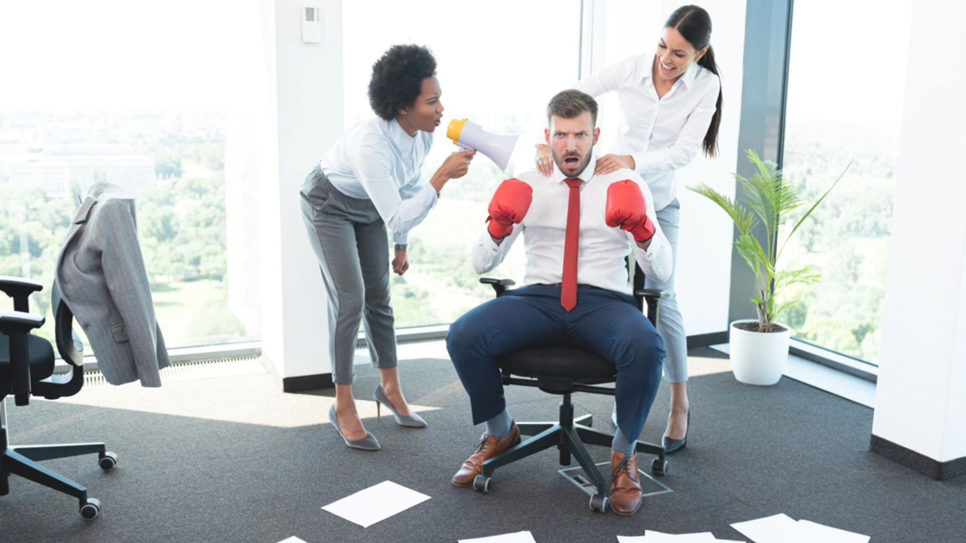 Business man wearing boxing gloves while female colleagues encourage him to fight