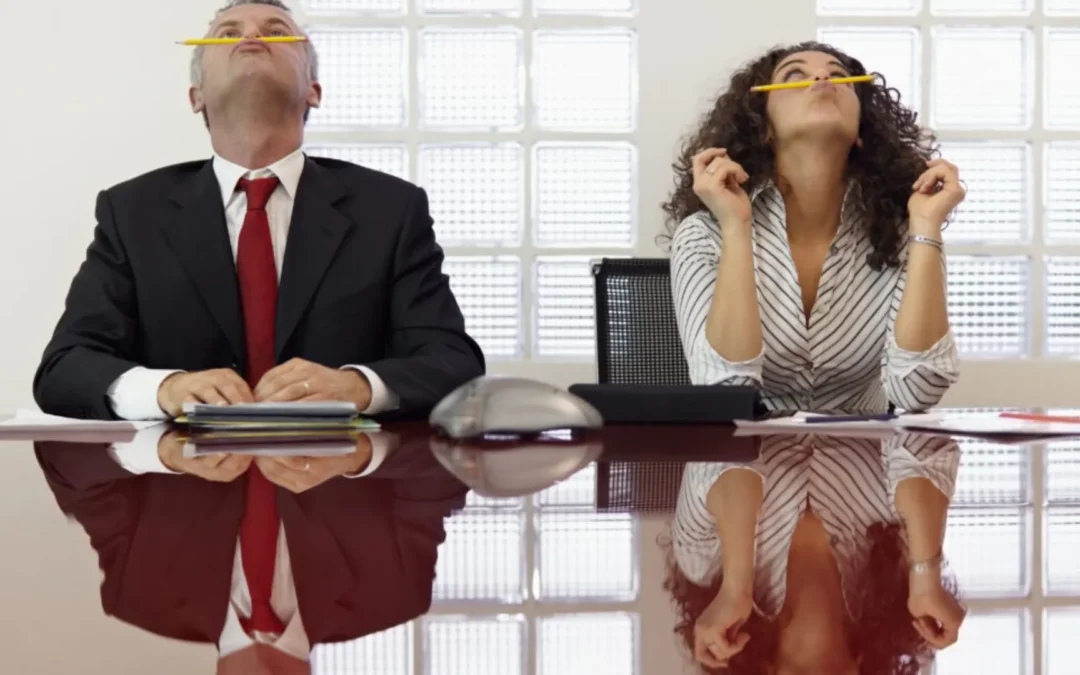 Two people in a meeting, bored and balancing pencils on their upper lips