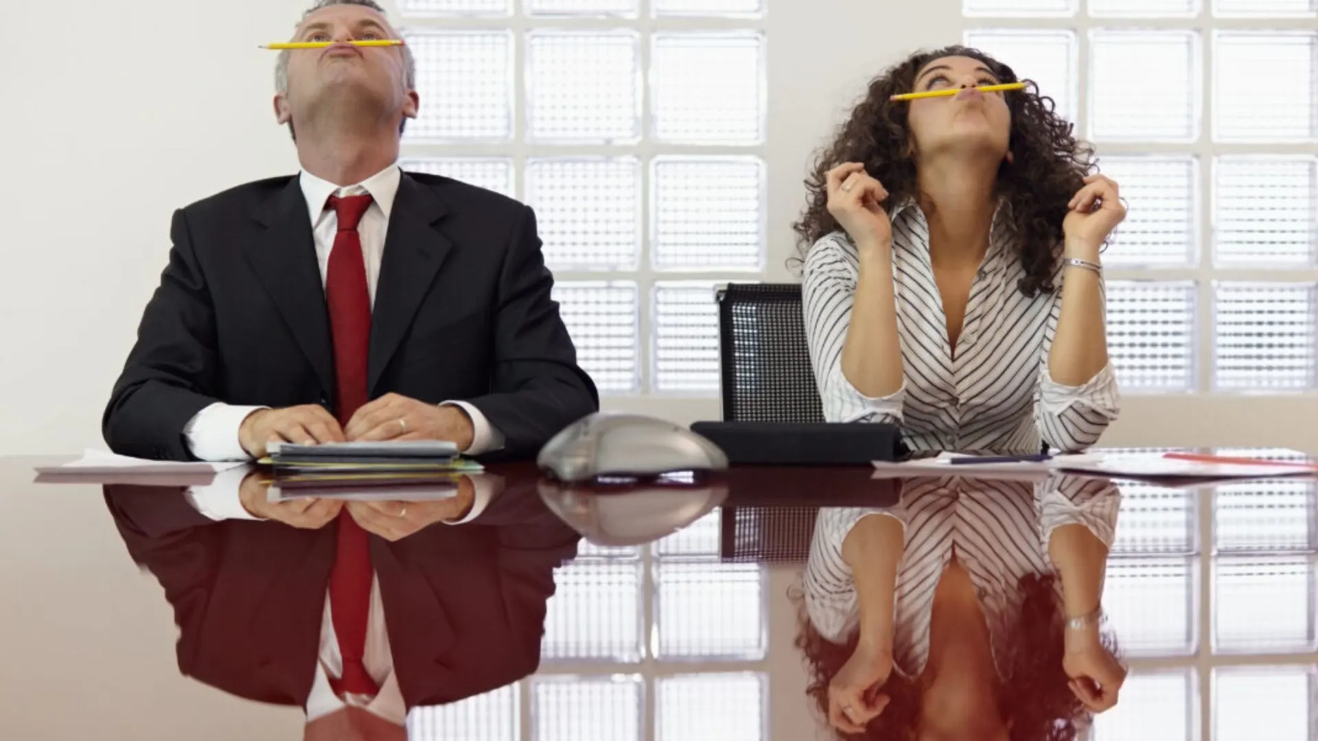 Two people in a meeting, bored and balancing pencils on their upper lips