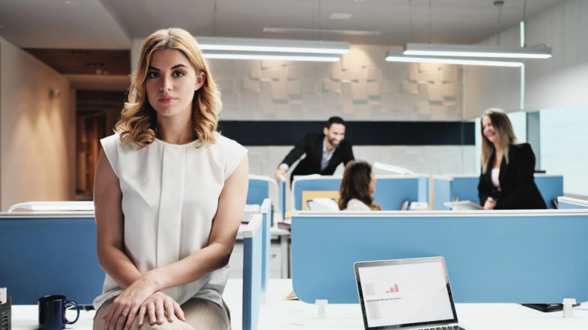 Woman sitting on desk alone while teammate talk without her