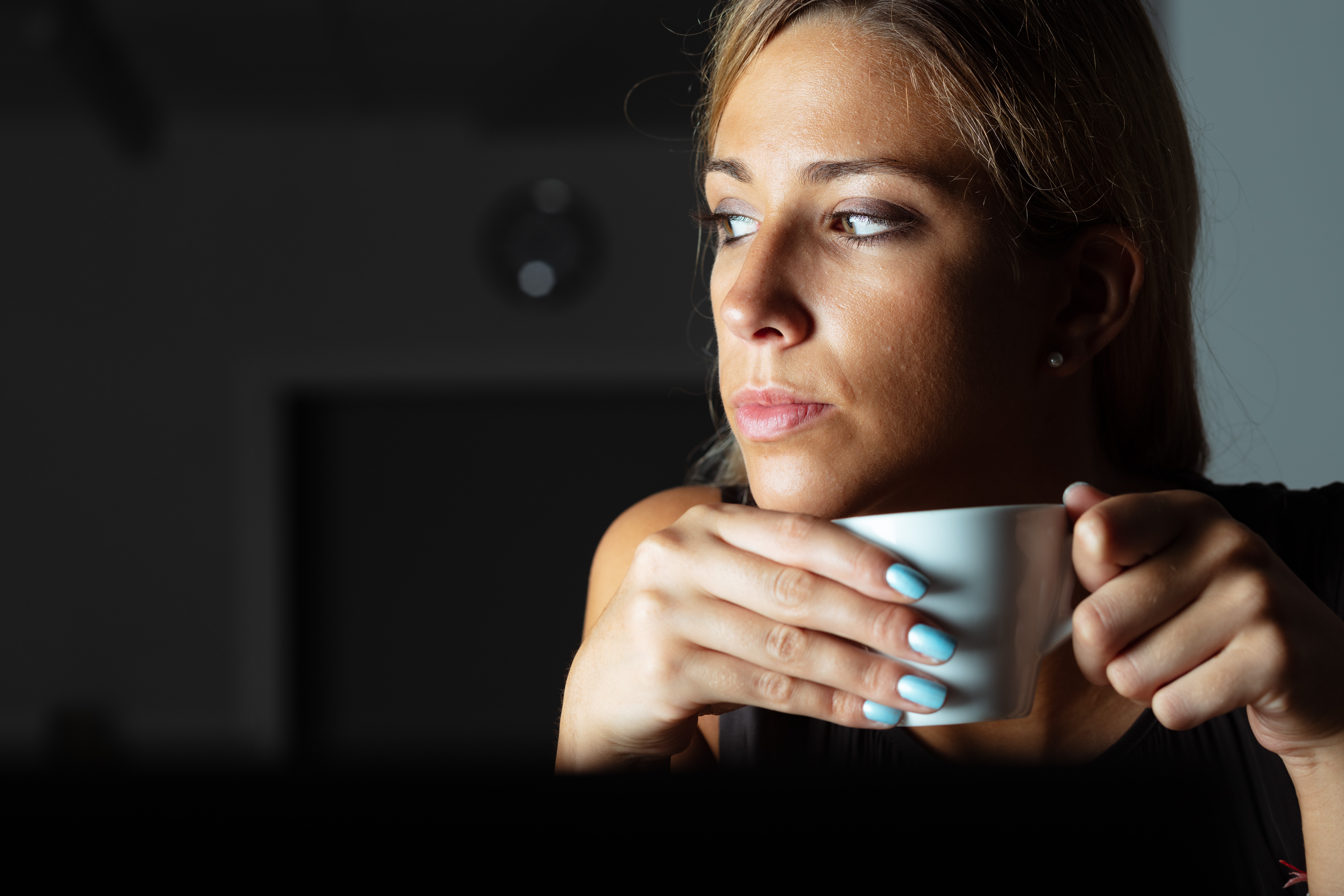 Person sitting in a dark office drinking coffee and looking pensively out the window