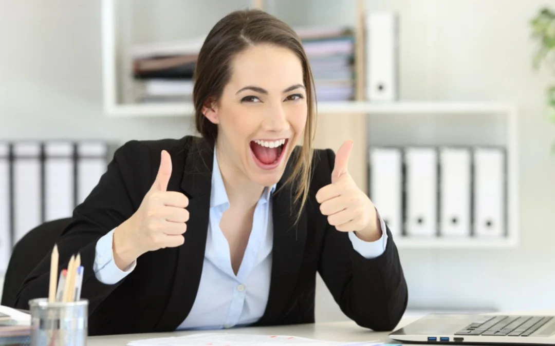Woman at desk giving enthusiastic two thumbs up