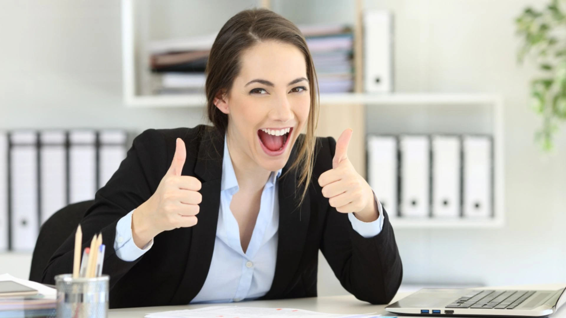 Woman at desk giving enthusiastic two thumbs up