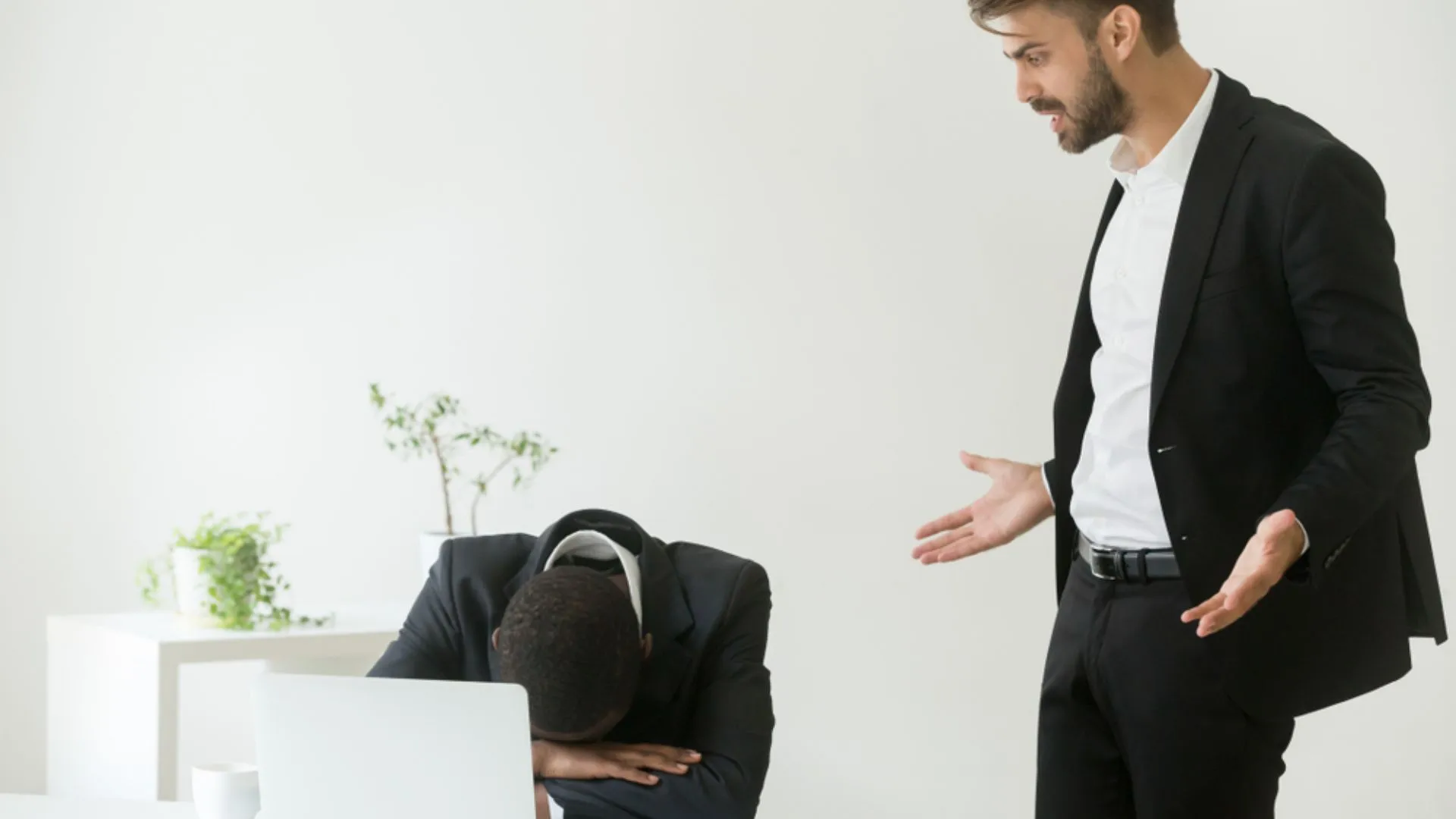 Employee with head down on desk while manager stands over looking frustrated