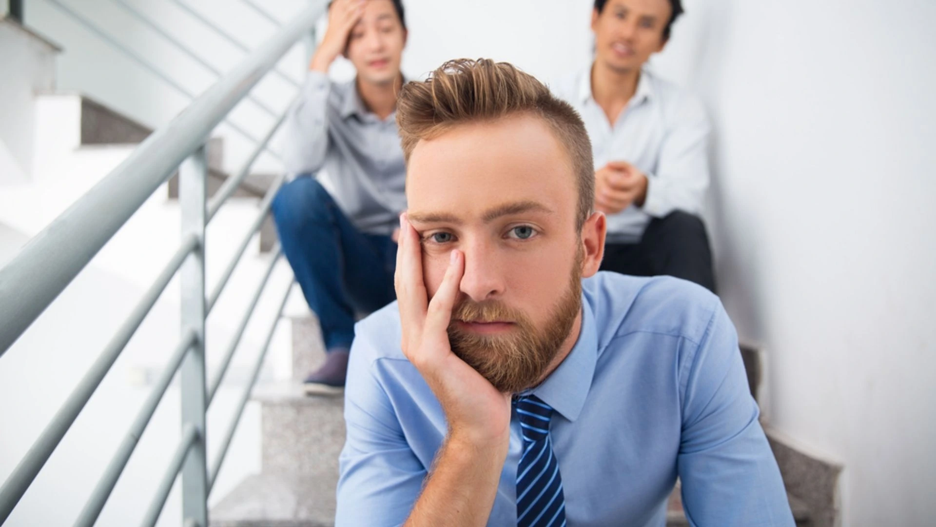 Three employees wearing work wear sitting on an industrial staircase looking unhappy