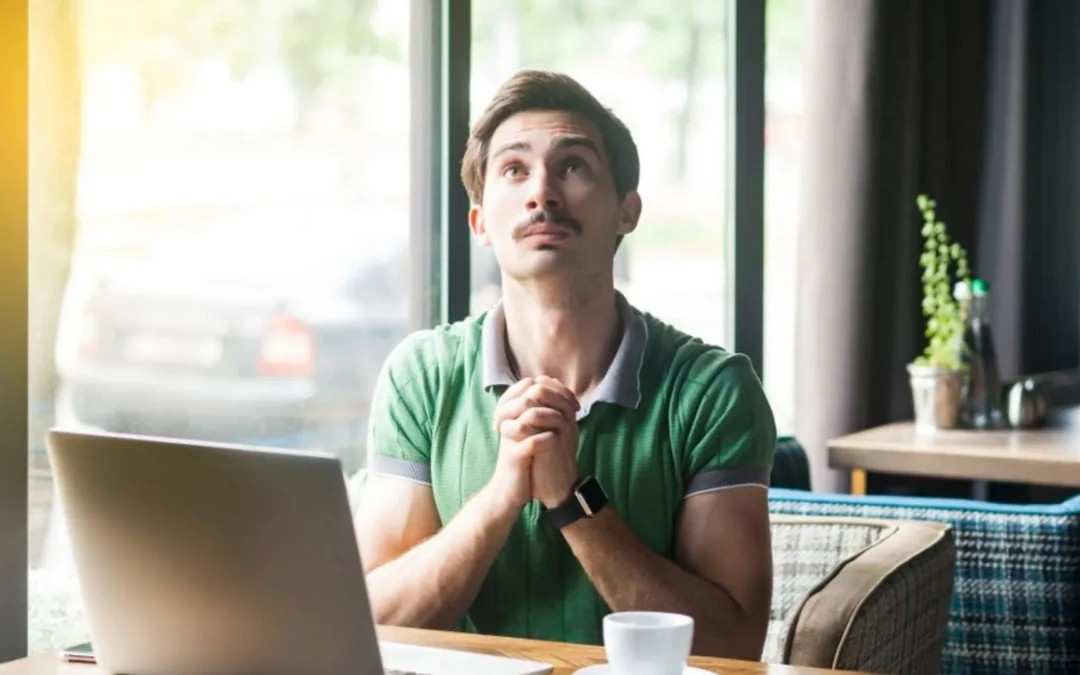 Man working on a laptop with hands crossed asking for foregiveness