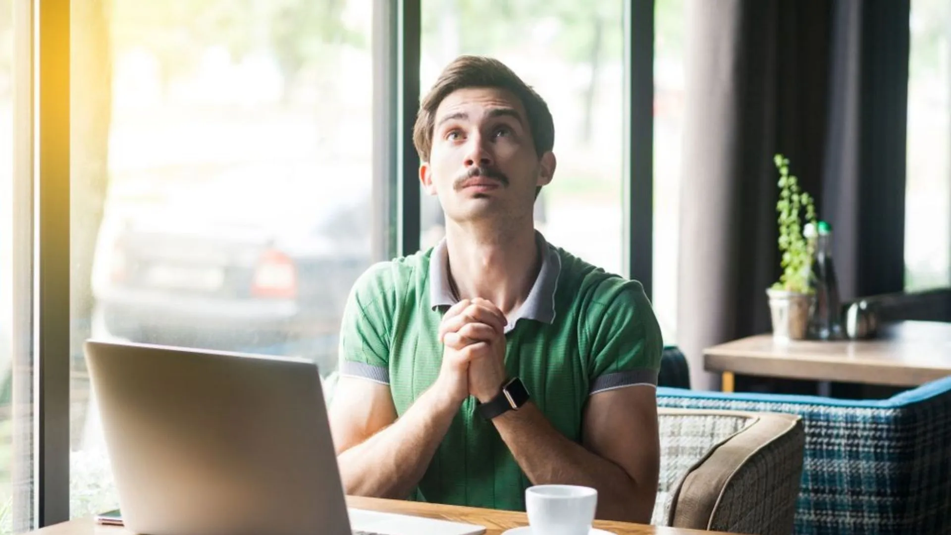Man working on a laptop with hands crossed asking for foregiveness