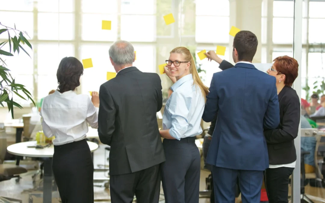 Woman looking at the camera while the boss and her team put sticky notes on the wall