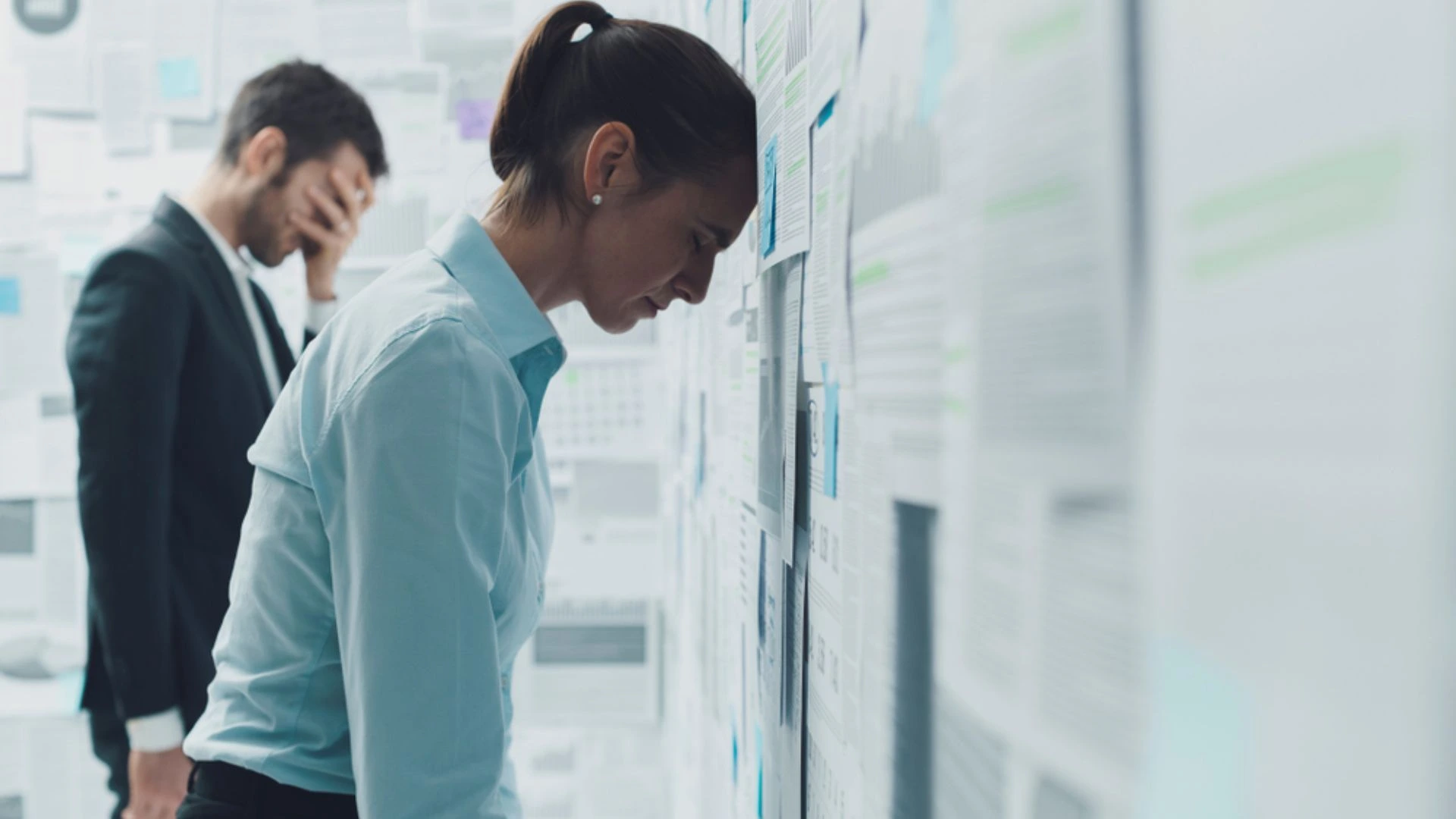 Woman with her head against a wall full of planning documents...giving up.