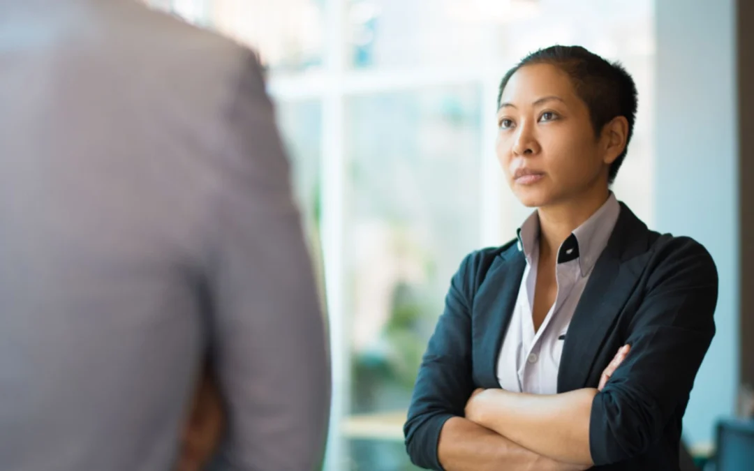 Woman with arms crossed looking dubious while talking to a colleague
