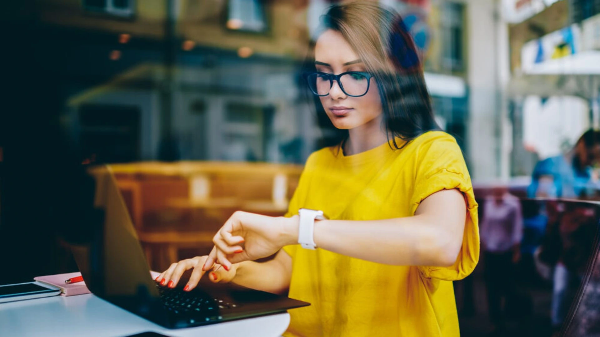 Woman in a cafe working on a laptop and looking at her watch doing time management