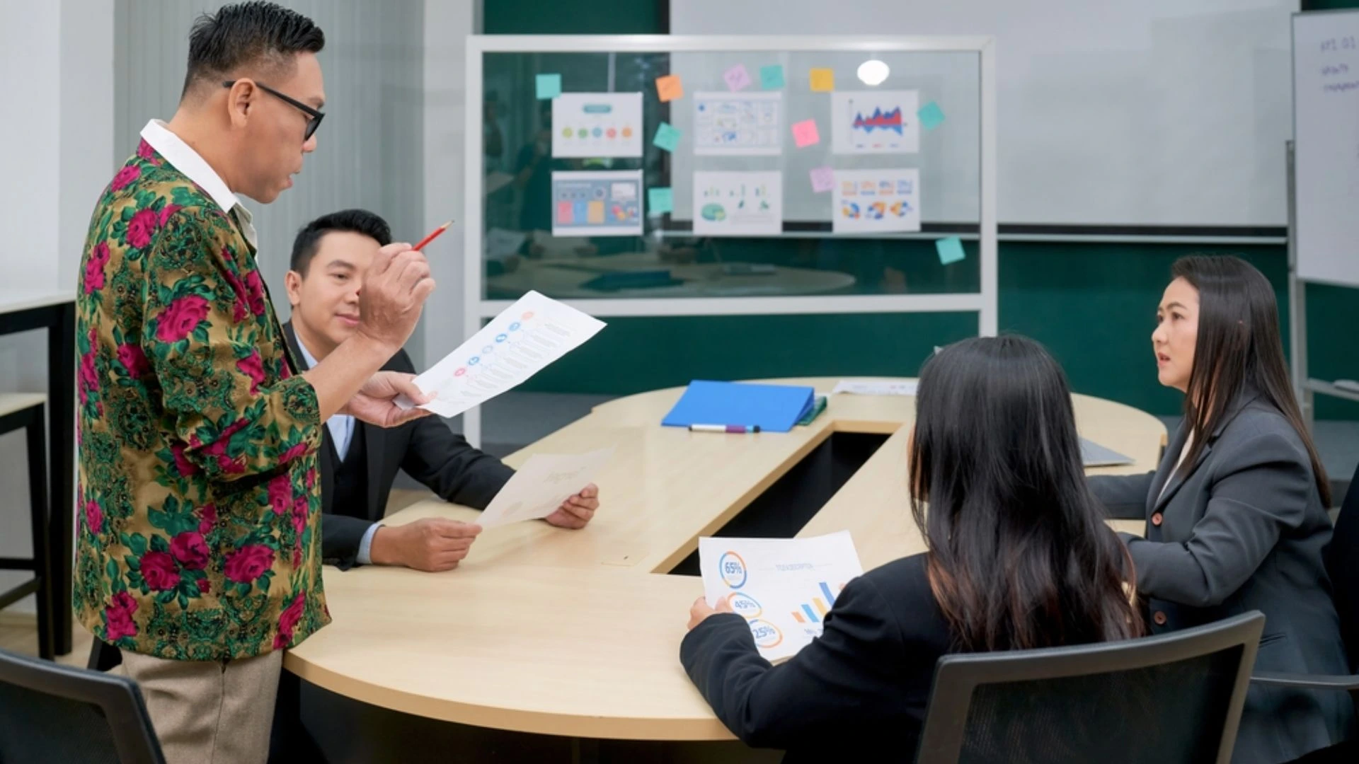 Team leader standing and talking to team who are seated around a table in a meeting