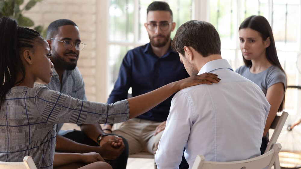 Person reaching out to put a hand on a shoulder of a colleague feeling sad.