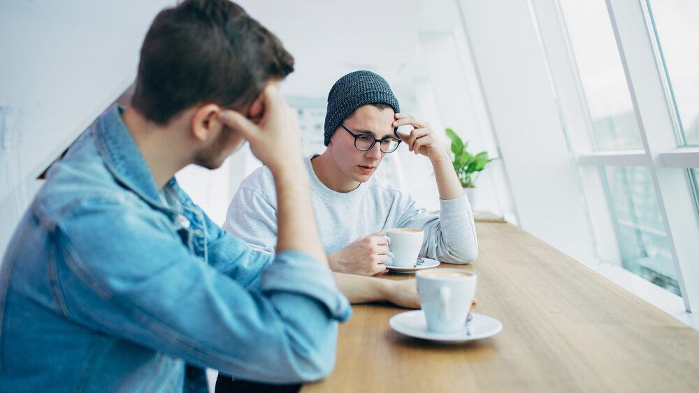 Two colleagues sitting having coffee. One colleague looks sad.