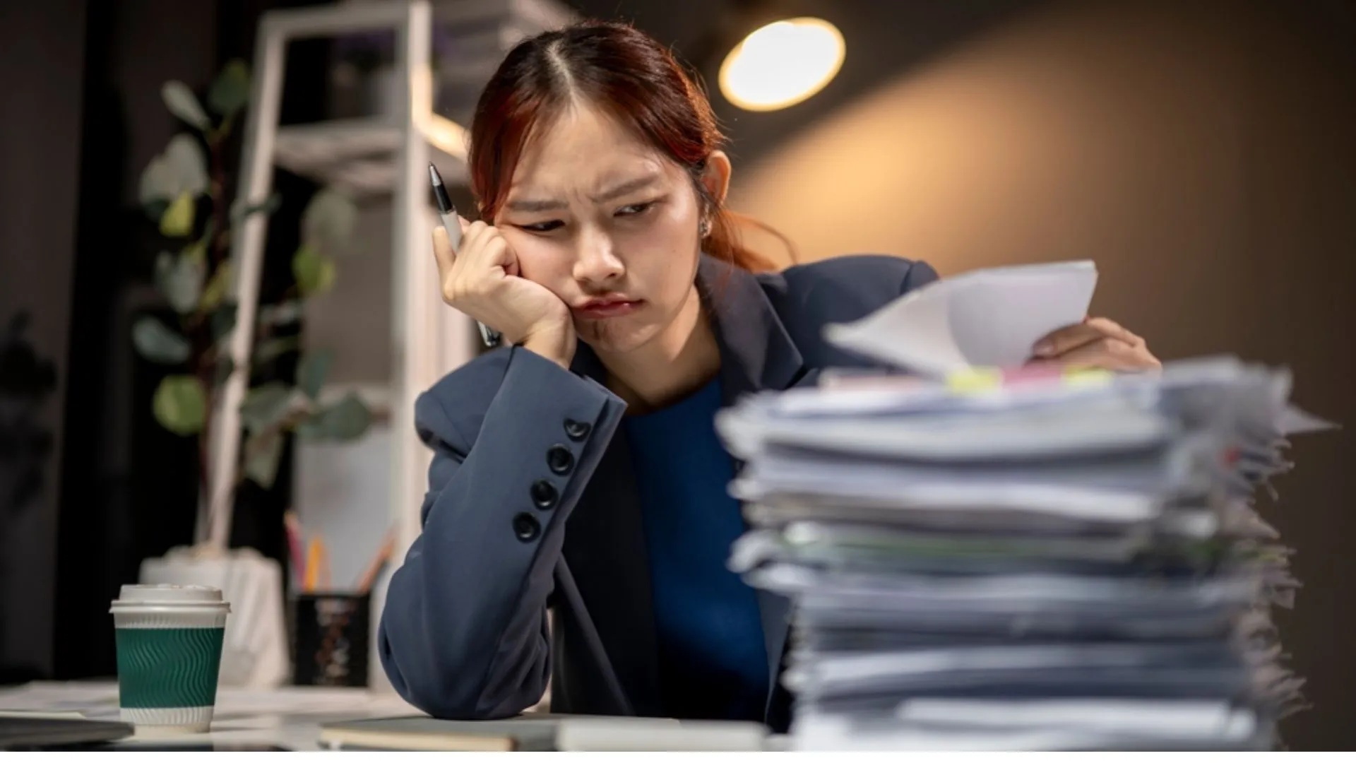 Woman looking exhausted sitting in front of a giant stack of work
