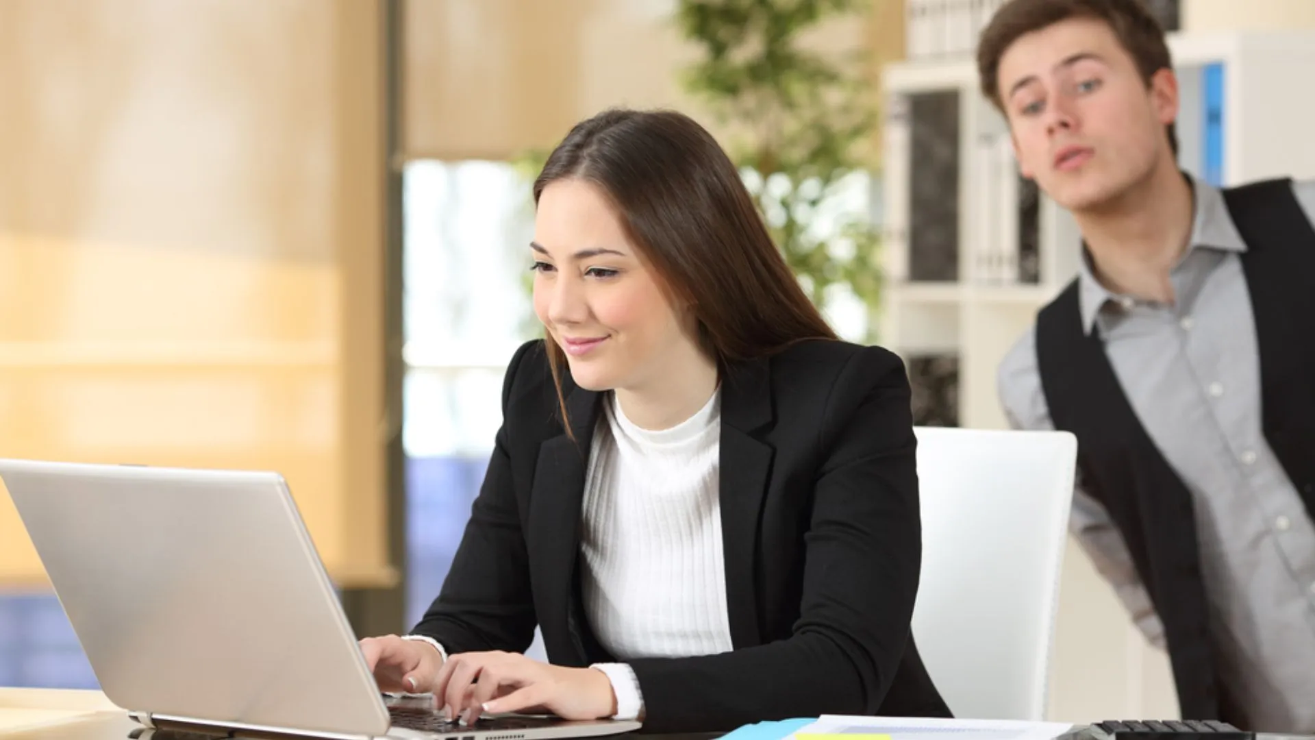 Woman working at her computer with a medding colleague looking over her shoulder