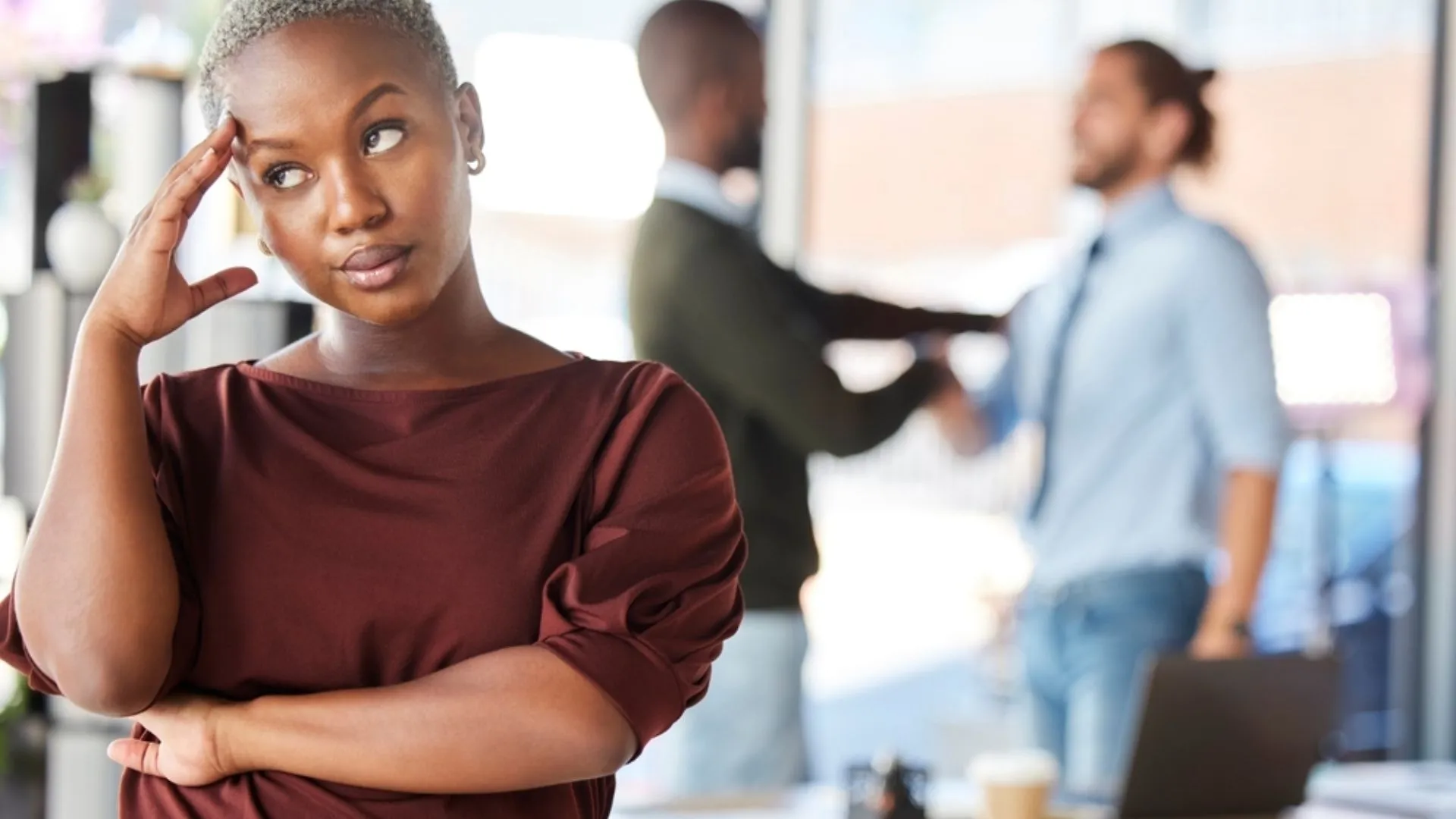 Woman rolling her eyes as two colleagues talk in the background