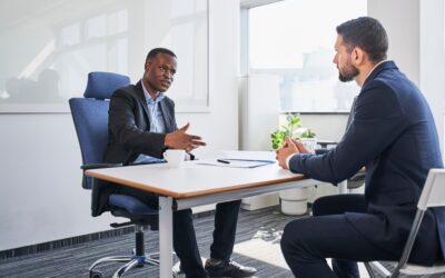 Two business men sitting across a desk from one another having a conversation