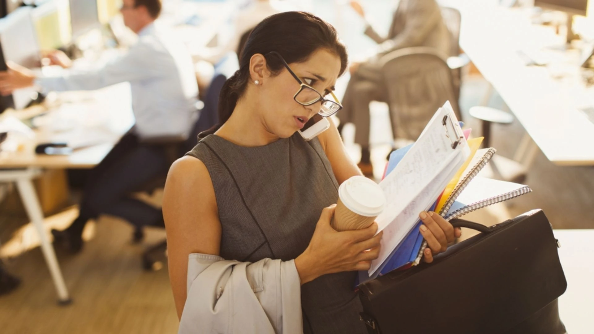 Woman talking on the phone while trying to carry a bunch of files because she's multitasking