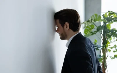 Man leaning his head against a white office wall dealing with too much work stress.