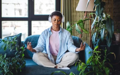 Woman wearing headphones and meditating in a plant-filled room to alleviate stress spillover
