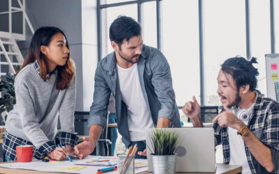 Three teammates standing over a desk having an argument. One being very dramatic