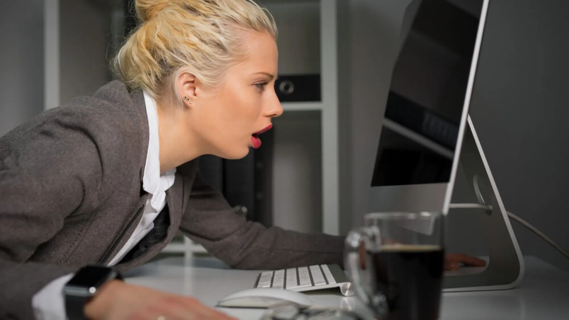 Woman with a giant coffee hunched over her computer looking like she's run out of energy