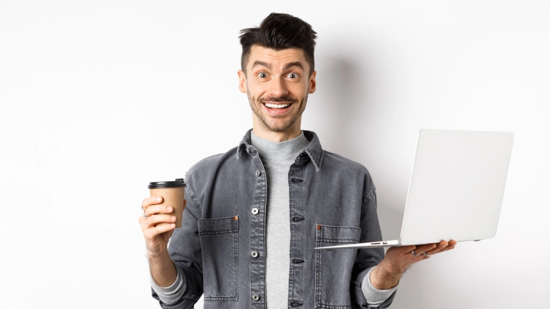 Man holding a laptop and a cup of coffee and looking enthusiastic