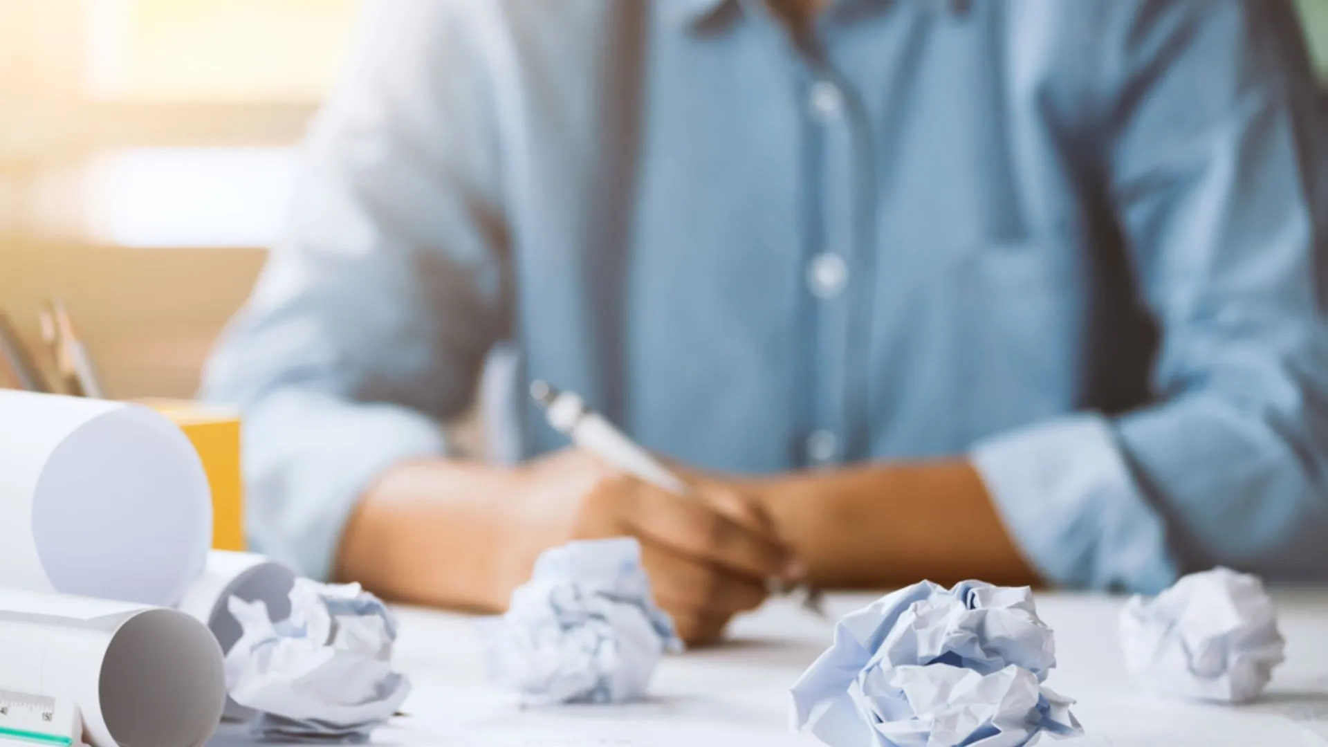 Person writing at their desk with lots of crumbled paper