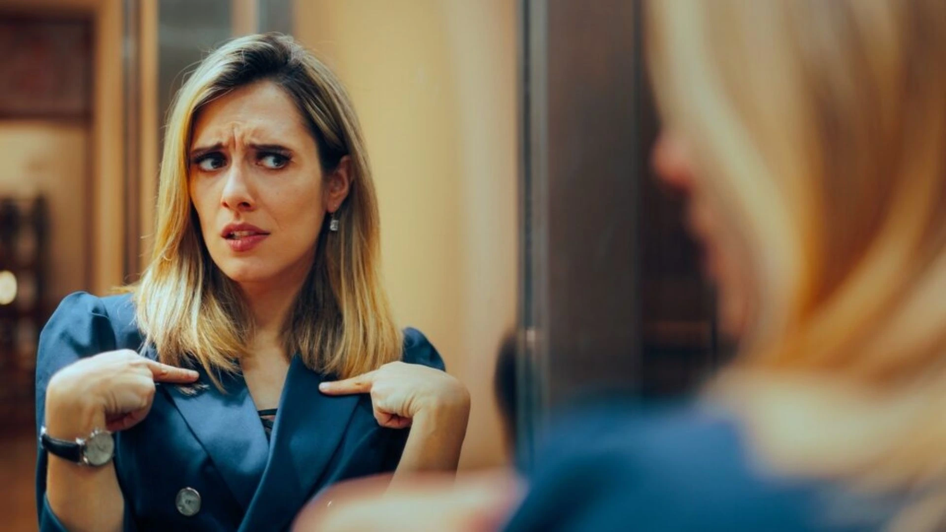 Woman looking in the mirror pointing at herself, questioning if it's about her